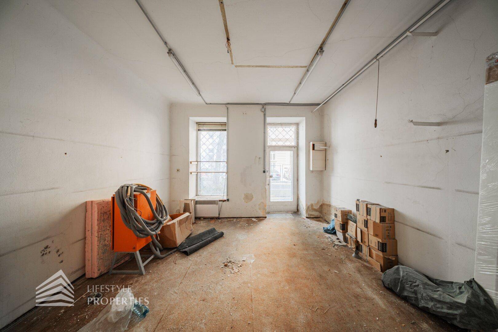 Unmöblierter Raum mit Fenster und Tür, bereit für den Ausbau, mit sichtbaren Baumaterialien.