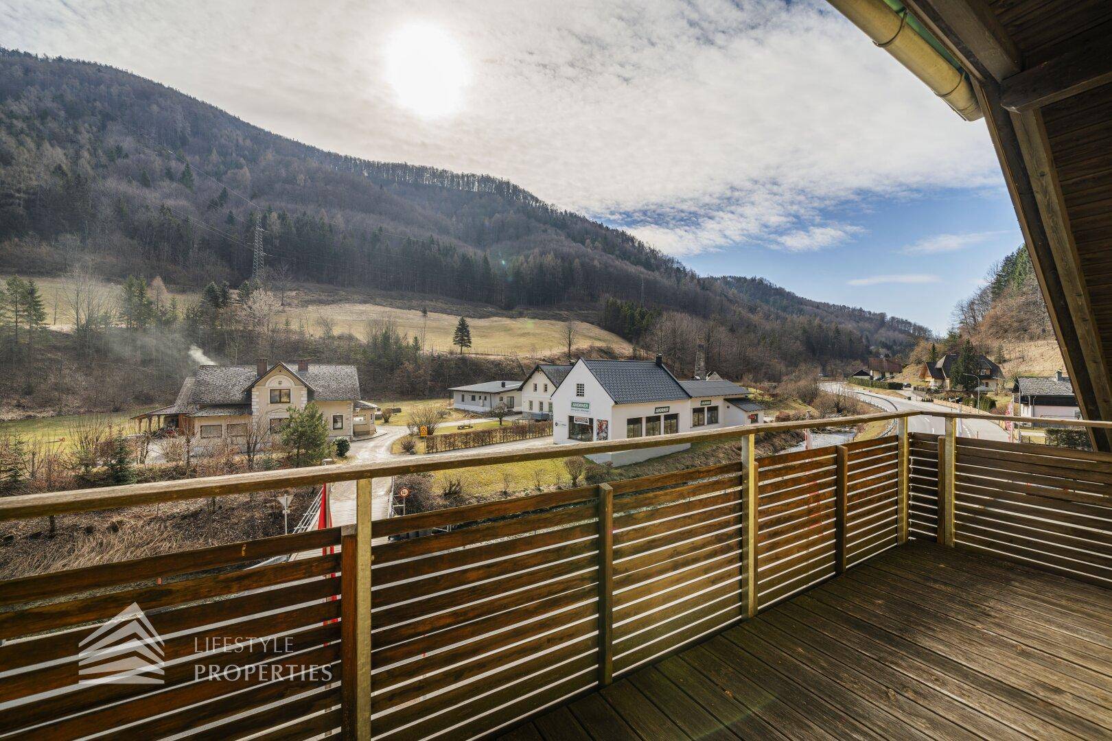 Balkon mit Holzboden und Bergblick über ein Tal mit Häusern.