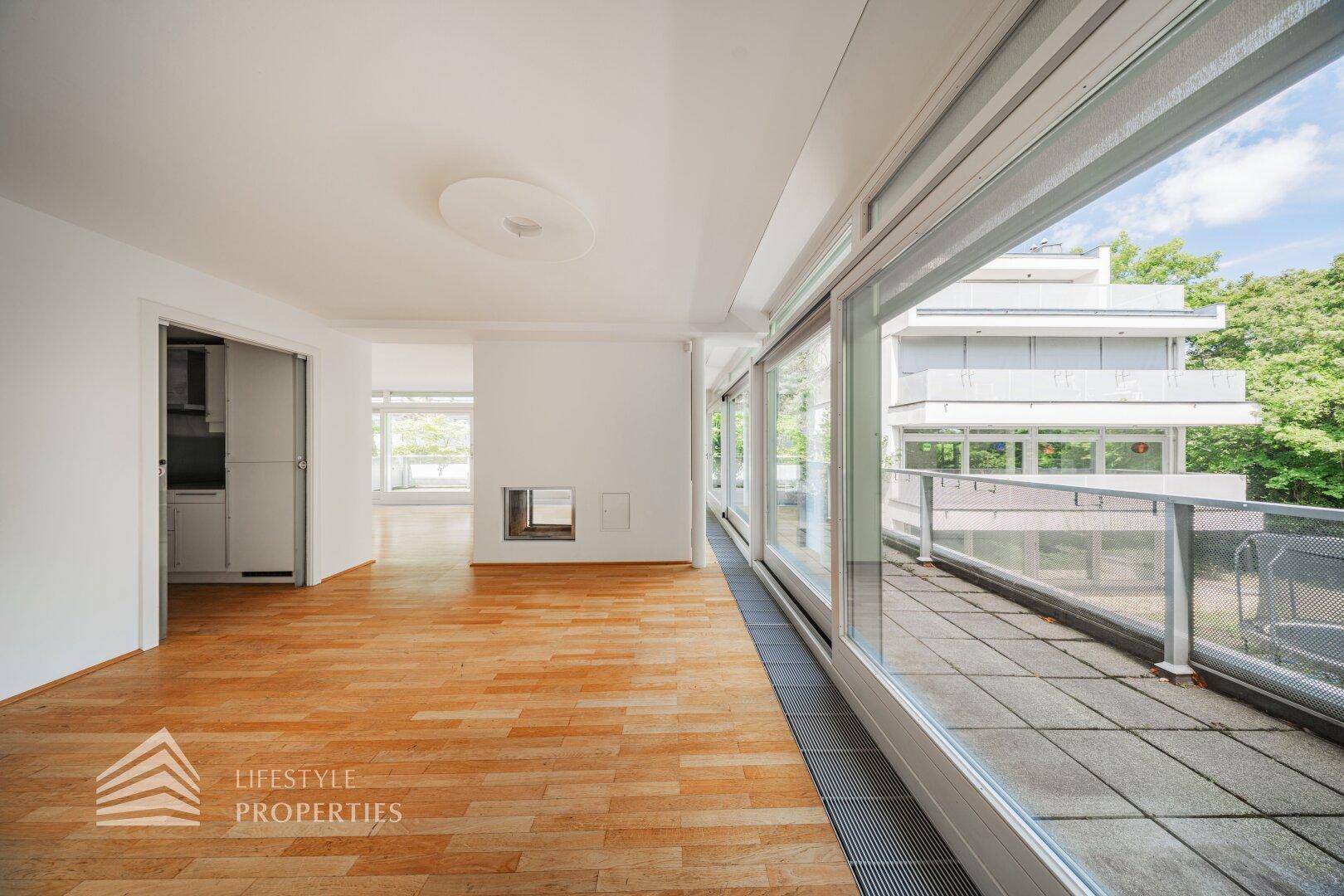 Wohnzimmer mit Holzboden, Kamin und Blick auf die angrenzende Küche und Terrasse.