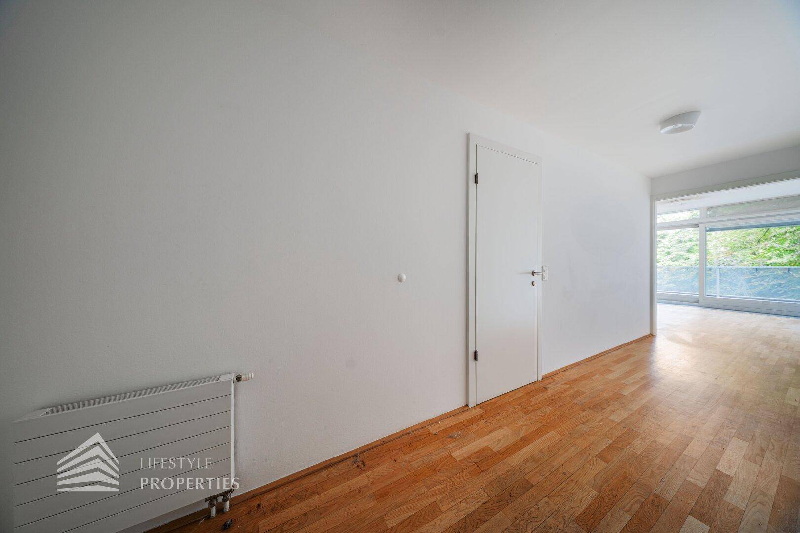 Schlichter Flur mit Holzboden, weißen Wänden und Zugang zu verschiedenen Räumen.