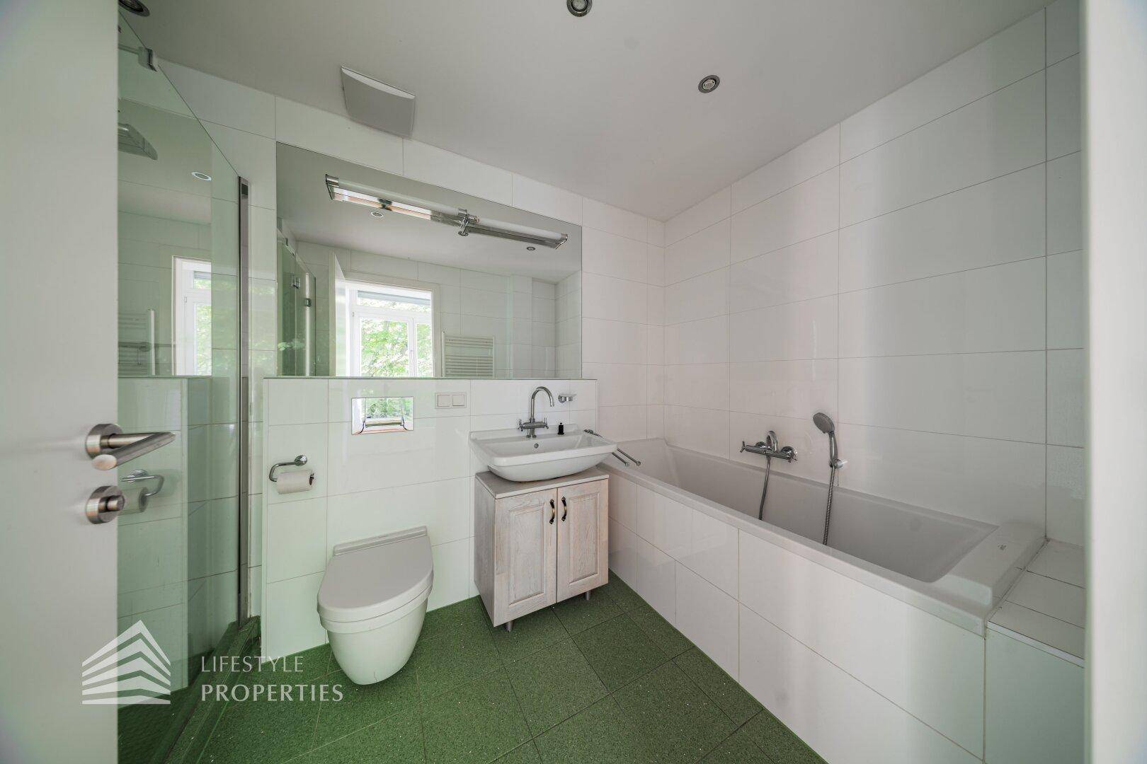 Badezimmer mit Badewanne, Dusche, wandhängender Toilette und grünem Fliesenboden.