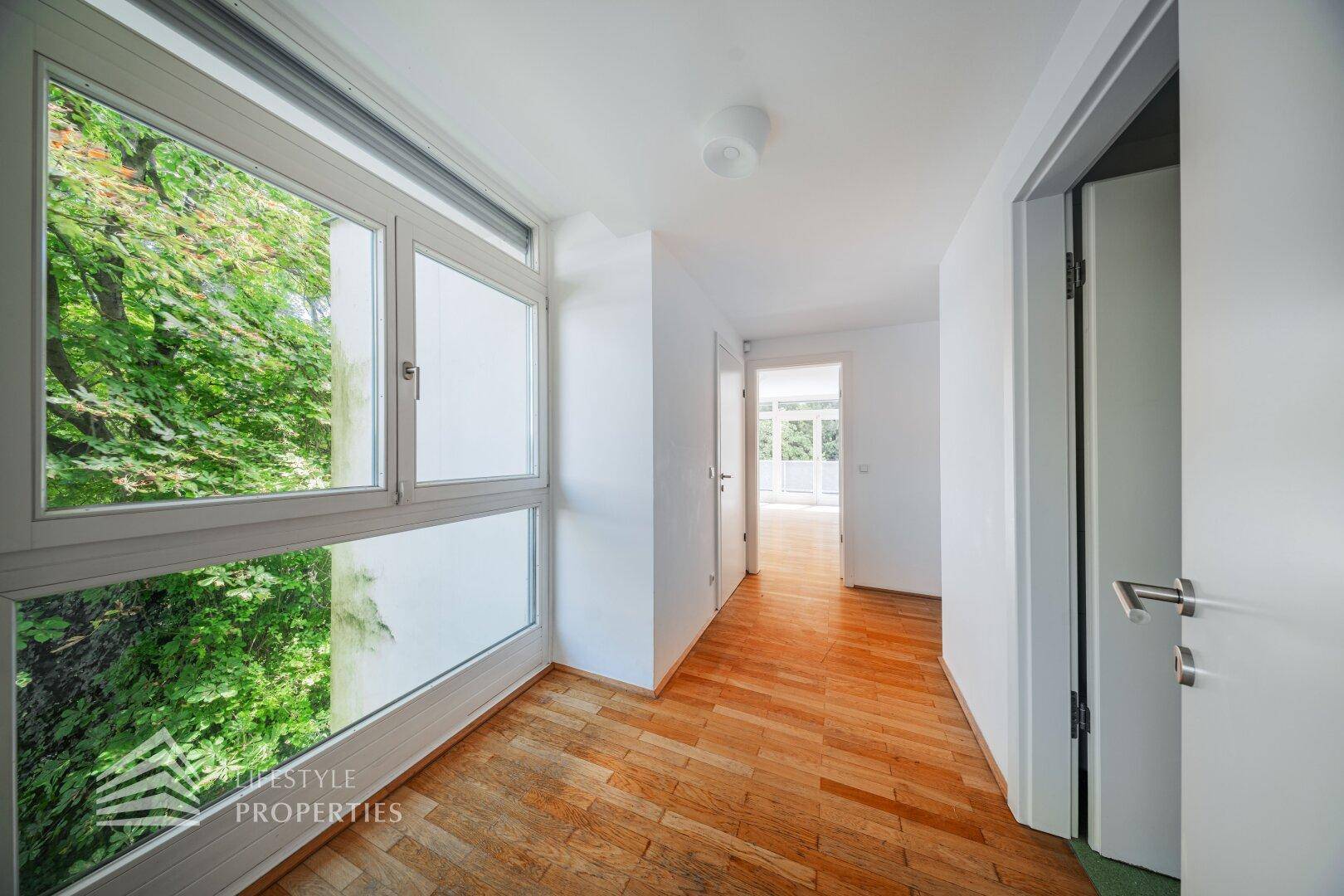 Heller Flur mit großem Fenster, Holzboden und Blick ins Grüne.