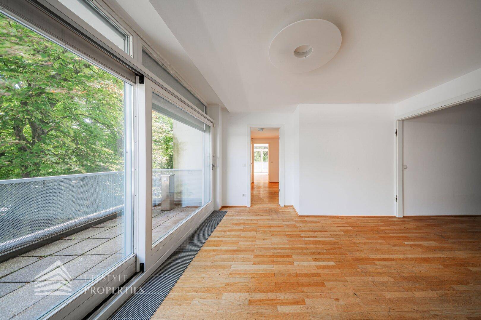 Heller Wohnbereich mit Holzboden und großzügigem Zugang zu einem weiteren Zimmer.