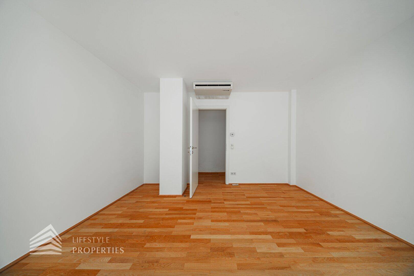 Schlafzimmer mit Holzboden, Klimaanlage und Zugang zu einem weiteren Raum.