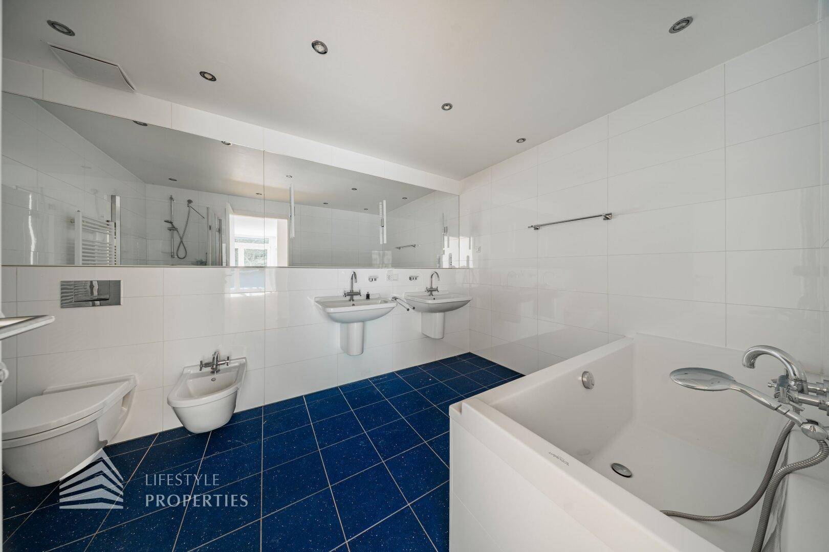 Großes Badezimmer mit Badewanne, Bidet, Doppelwaschbecken und blauen Fliesen.