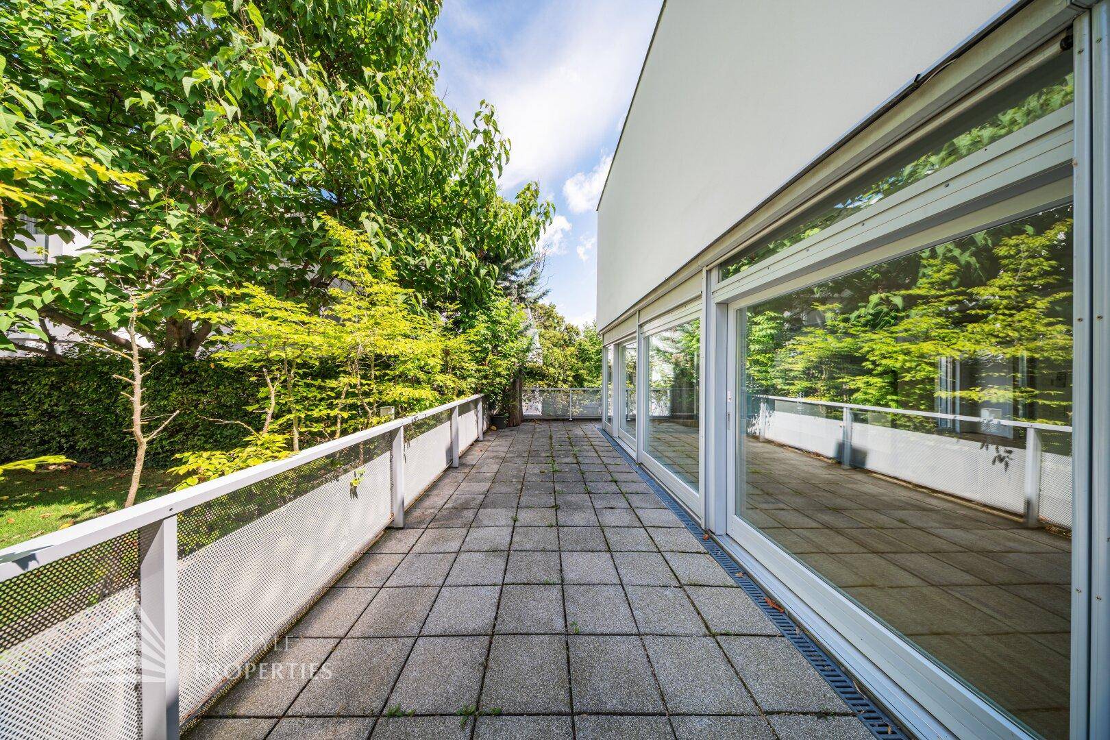 Breite Terrasse mit Steinplatten und Blick auf den Garten, umgeben von Bäumen und Sträuchern.