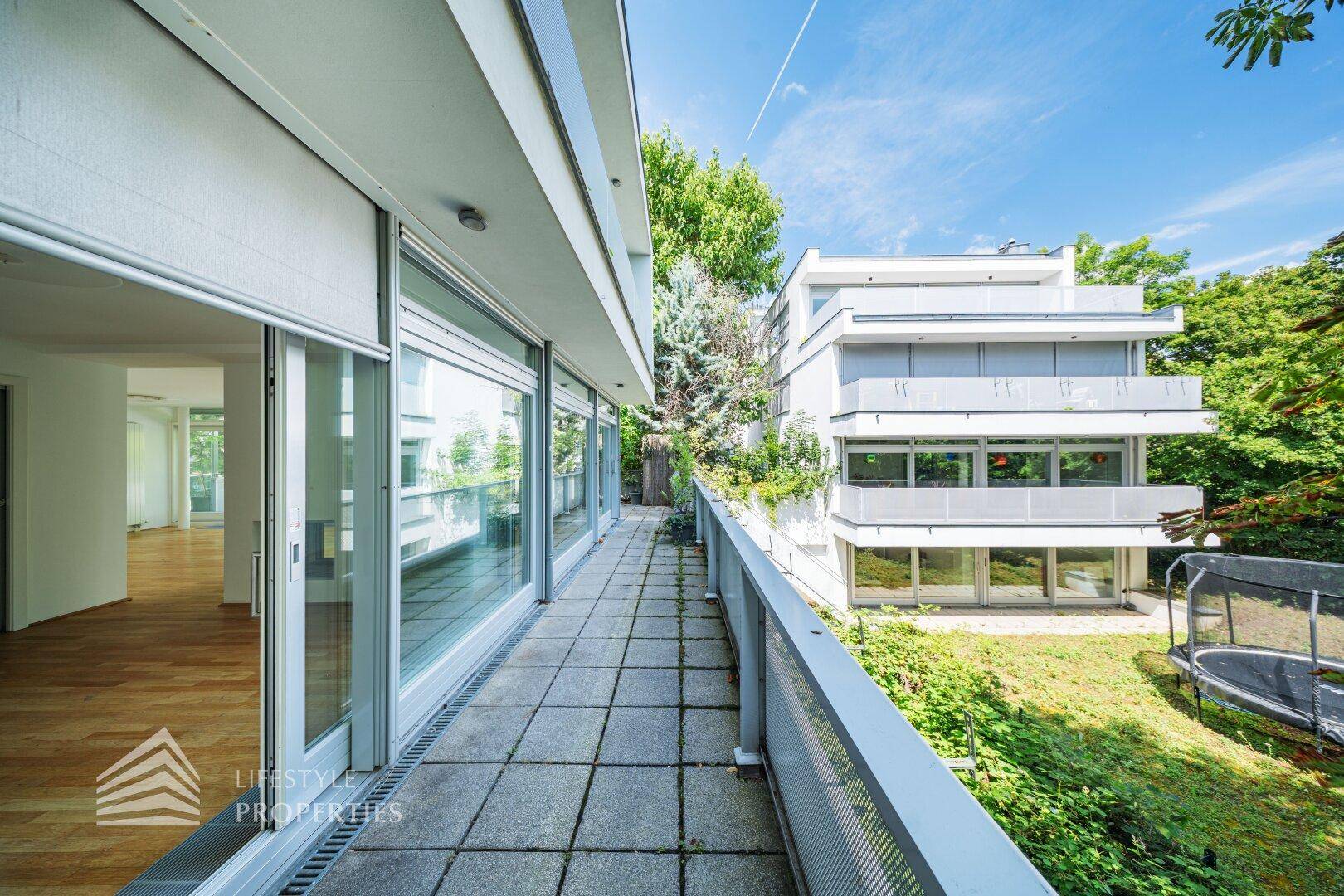 Lange Terrasse mit Steinplatten und Blick auf ein benachbartes Gebäude und den Gartenbereich.