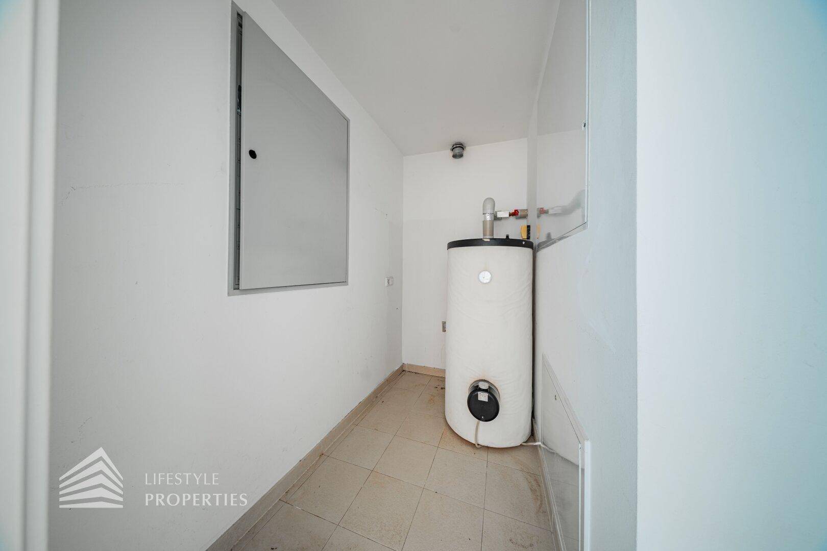 Funktionaler Hauswirtschaftsraum mit Warmwasserbereiter und Fliesenboden.