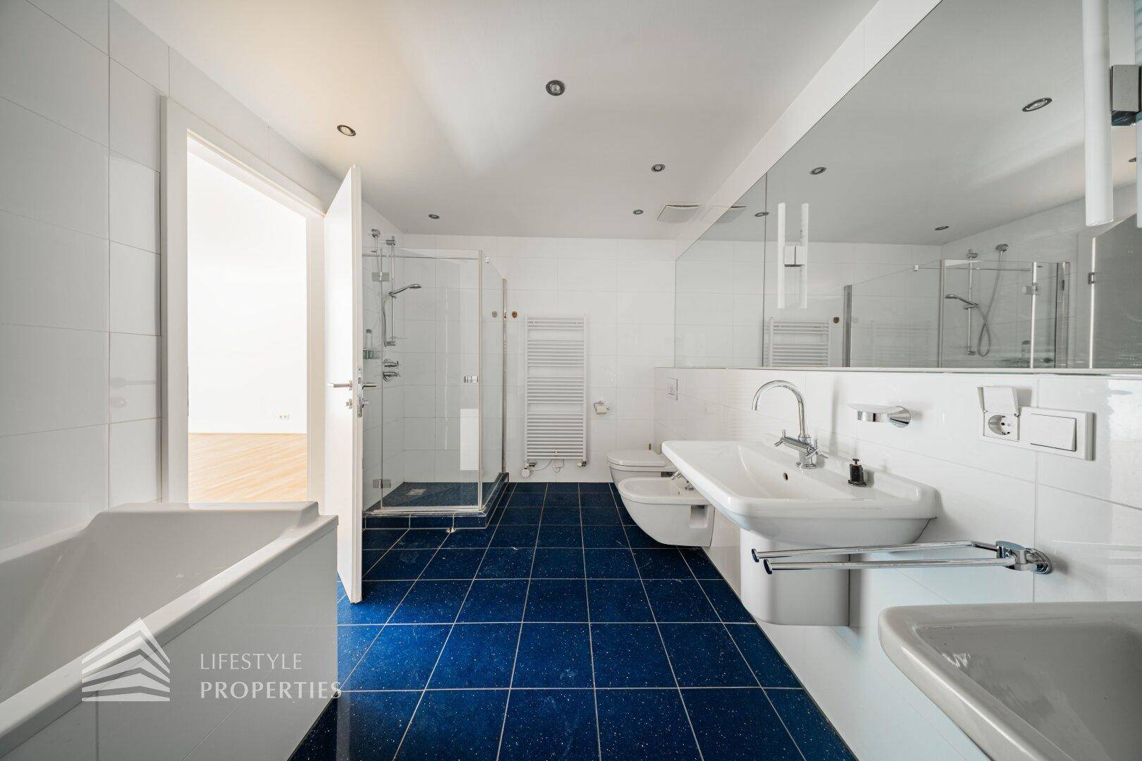 Geräumiges Badezimmer mit Badewanne, Dusche, Bidet, Doppelwaschbecken und blauen Fliesen.