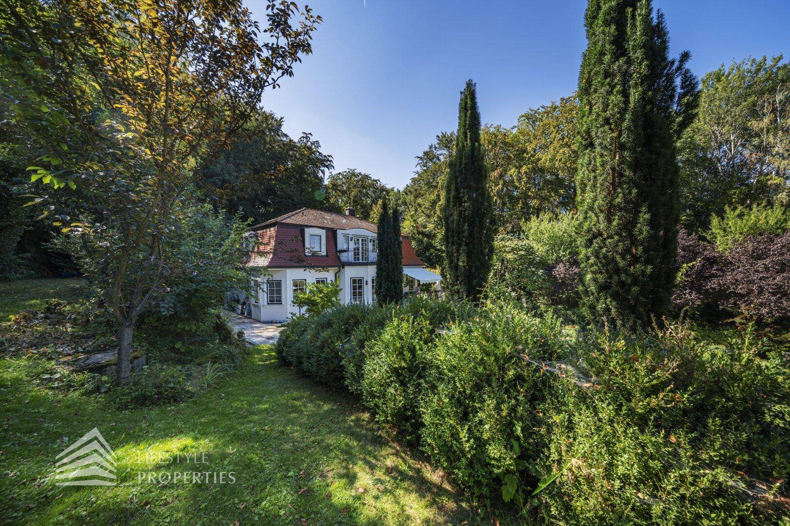 Elegantes Haus umgeben von einem weitläufigen, gepflegten Garten mit hohen Bäumen.