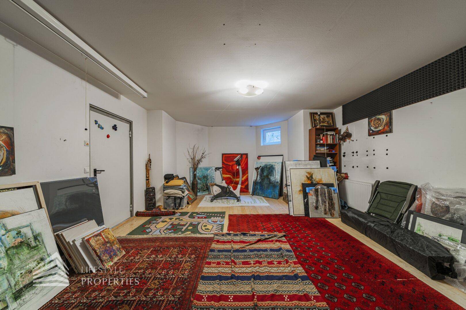 Vielseitiger Kellerraum, genutzt als Atelier und Lagerfläche, mit Teppichen und Kunstwerken.