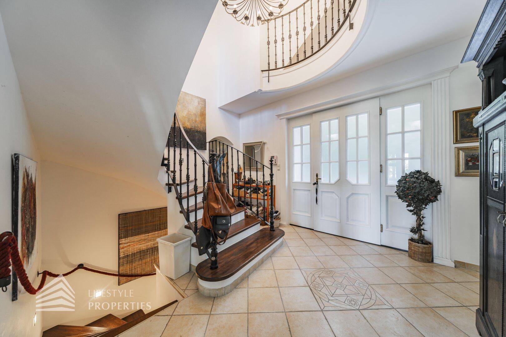 Elegante Eingangshalle mit geschwungener Treppe, kunstvollem Geländer und hellem Fliesenboden.