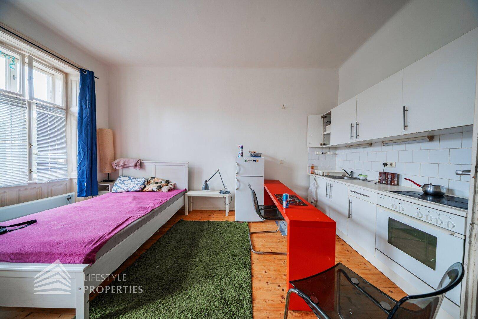 Integrierte Küchenzeile mit weißen Schränken, Herd und Kühlschrank im Studio-Apartment.