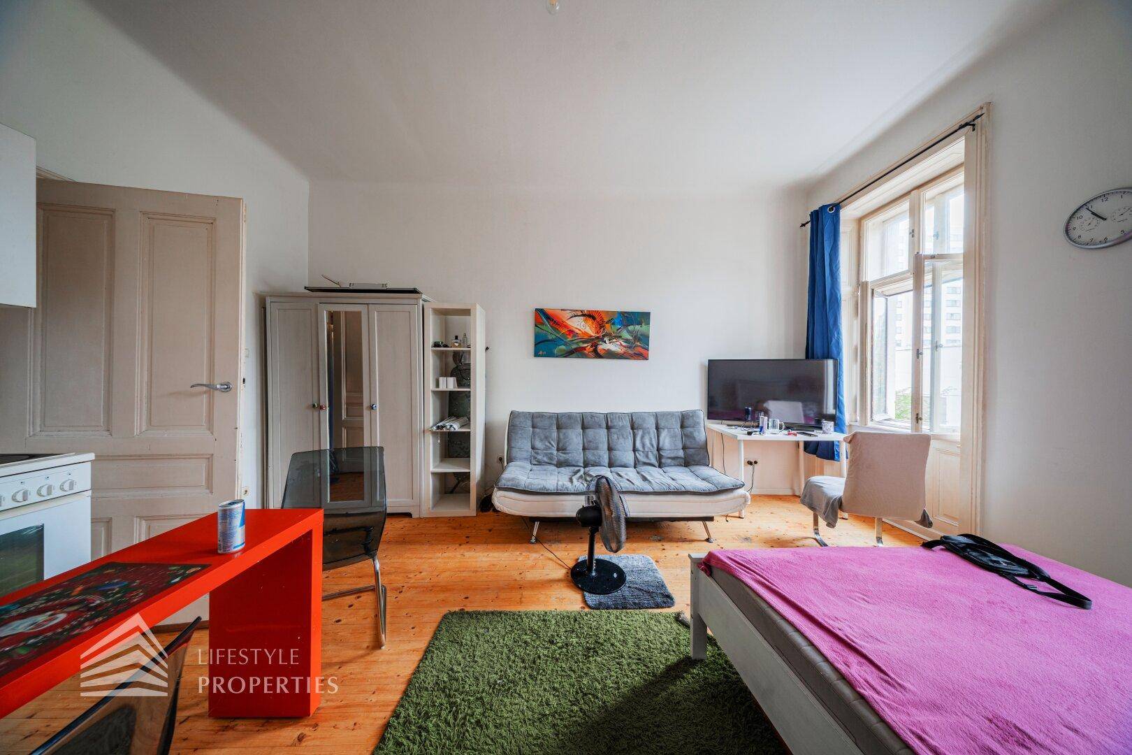 Gemütlicher Wohnbereich mit Schlafgelegenheit, Sofa und Kleiderschrank auf Holzdielenboden.