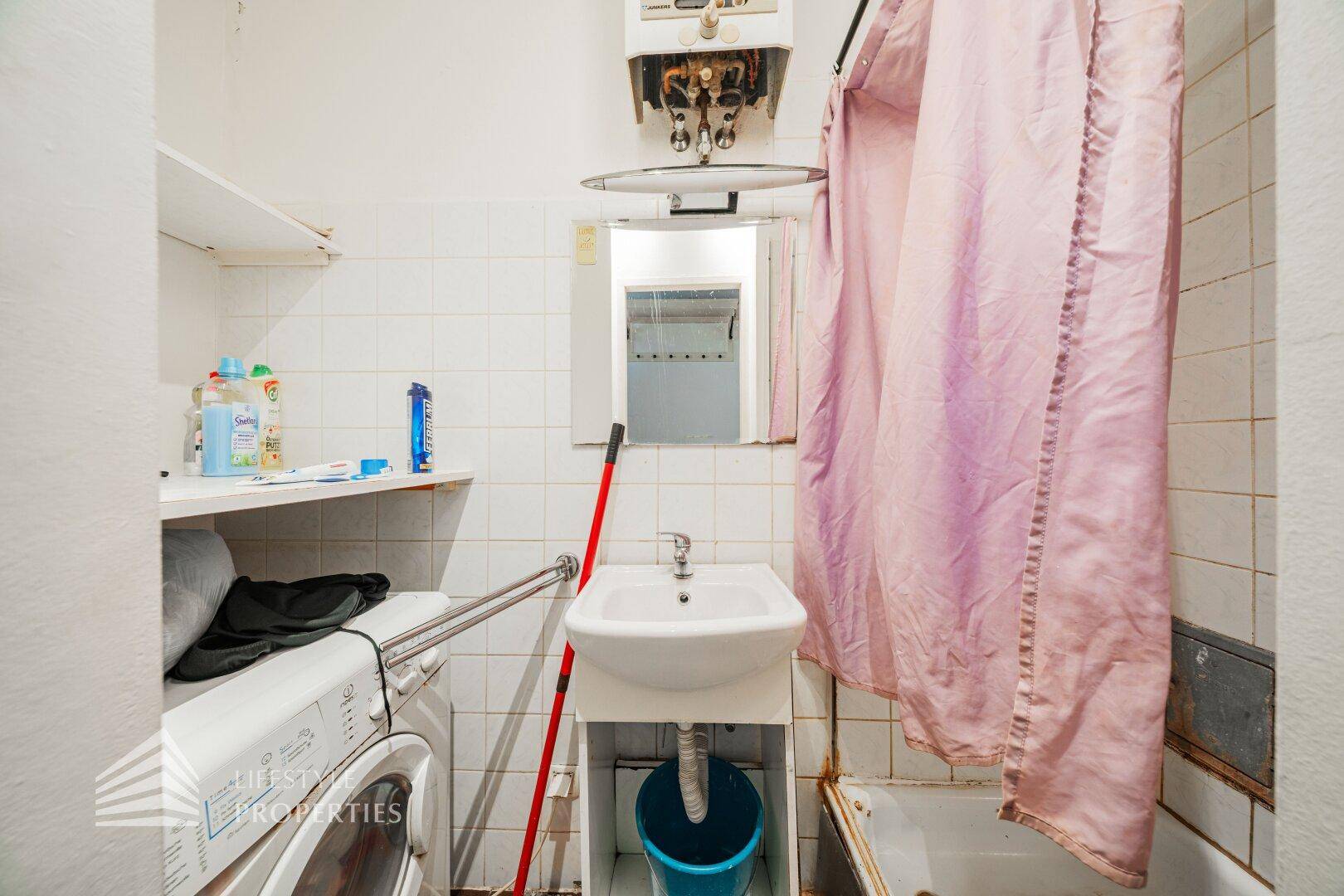 Kleines Badezimmer mit Badewanne, Waschbecken, Waschmaschine und weißen Wandfliesen.