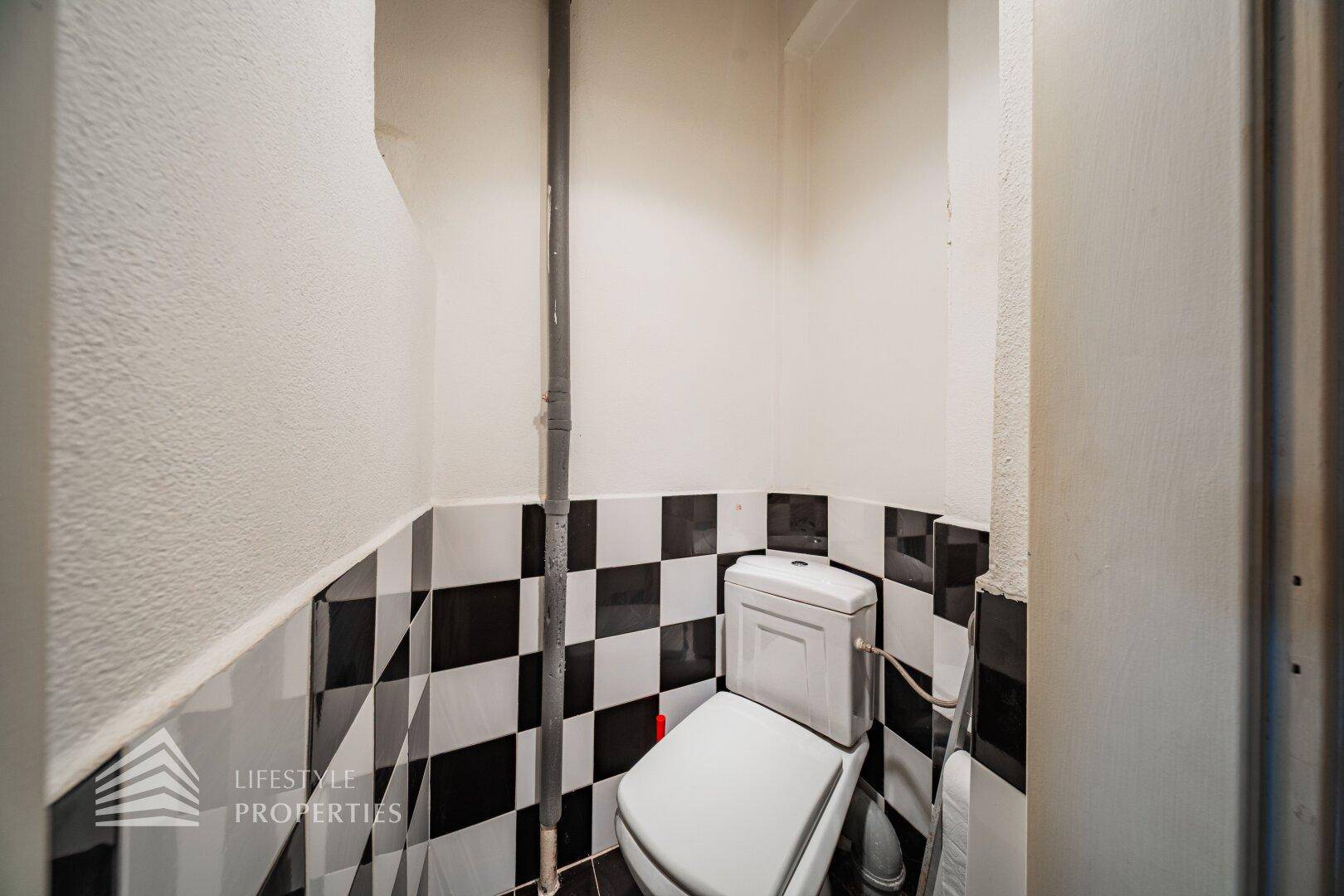Separate Toilette mit markanten schwarz-weiß karierten Fliesen und einfacher Ausstattung.