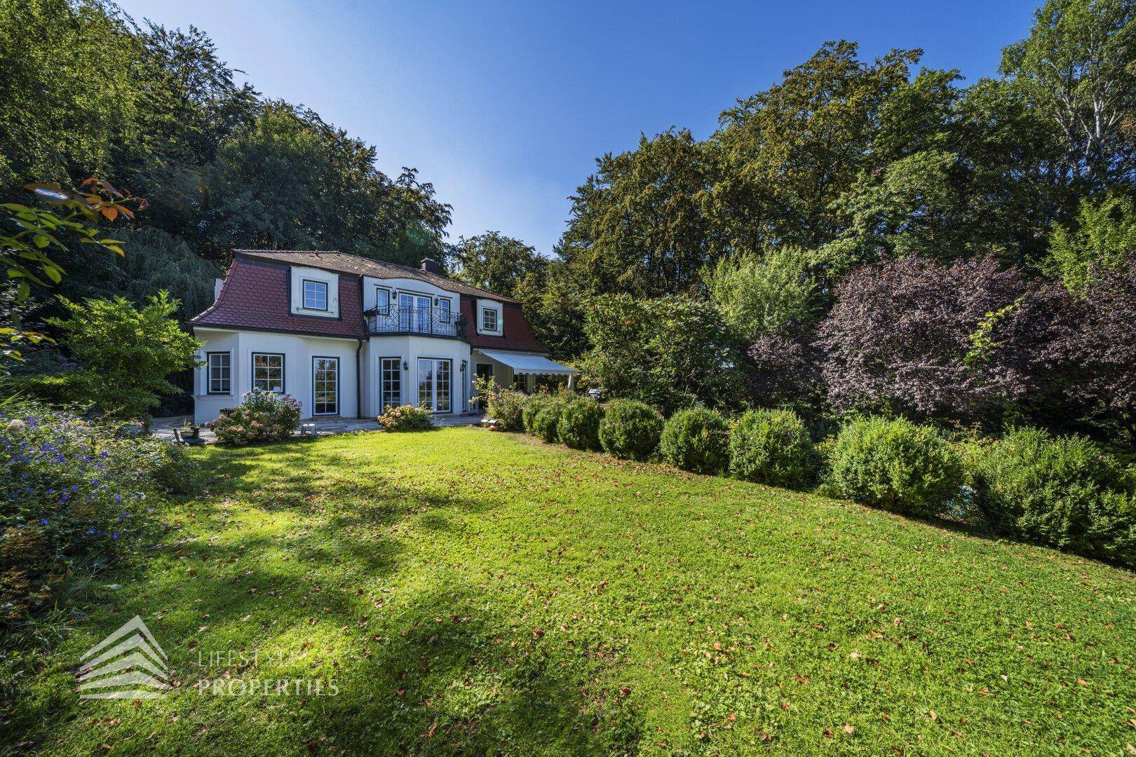 Charmante Villa mit weitläufigem Rasen und gepflegter Gartenlandschaft unter blauem Himmel.