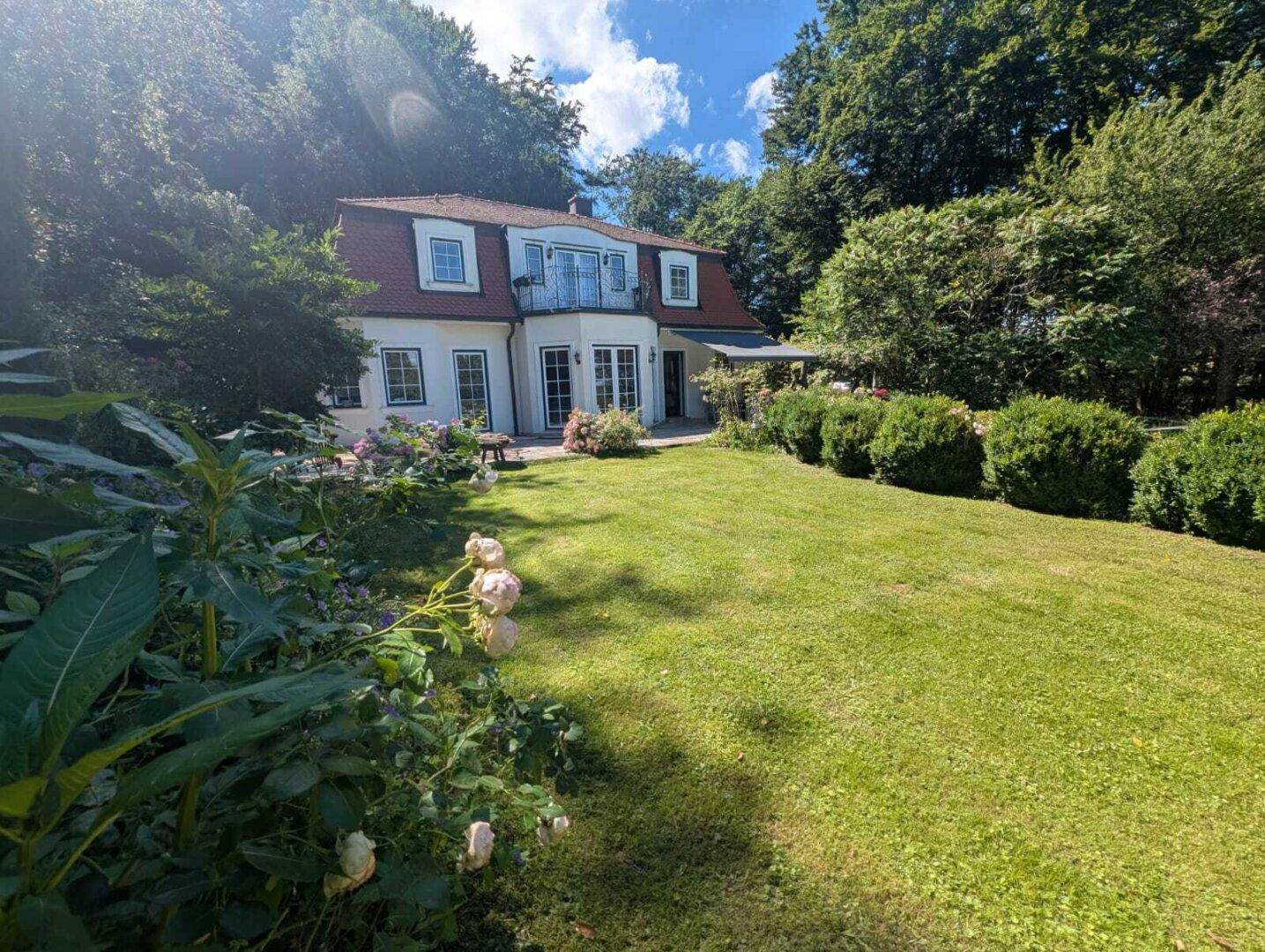 Großzügiger Garten mit Rasenfläche und blühenden Pflanzen vor dem eleganten Haus.