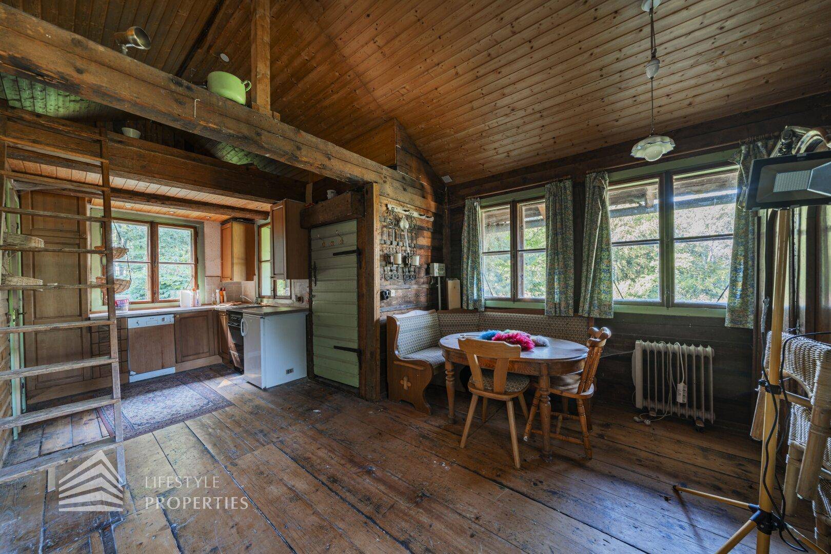Gemütlicher Wohn-Essbereich mit Holzboden und kleiner Küchenzeile im Hintergrund.