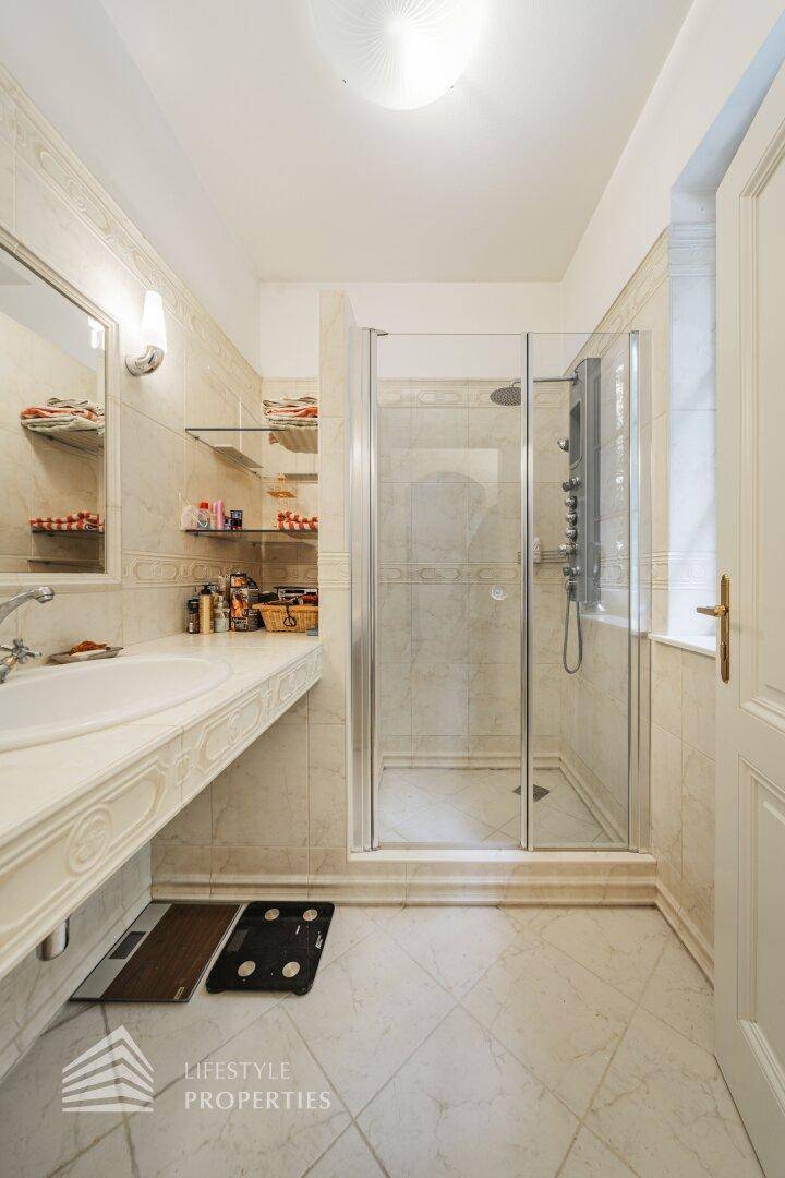 Helles Badezimmer mit Dusche, Einzelwaschbecken und hellen Fliesen an Wänden und Boden.