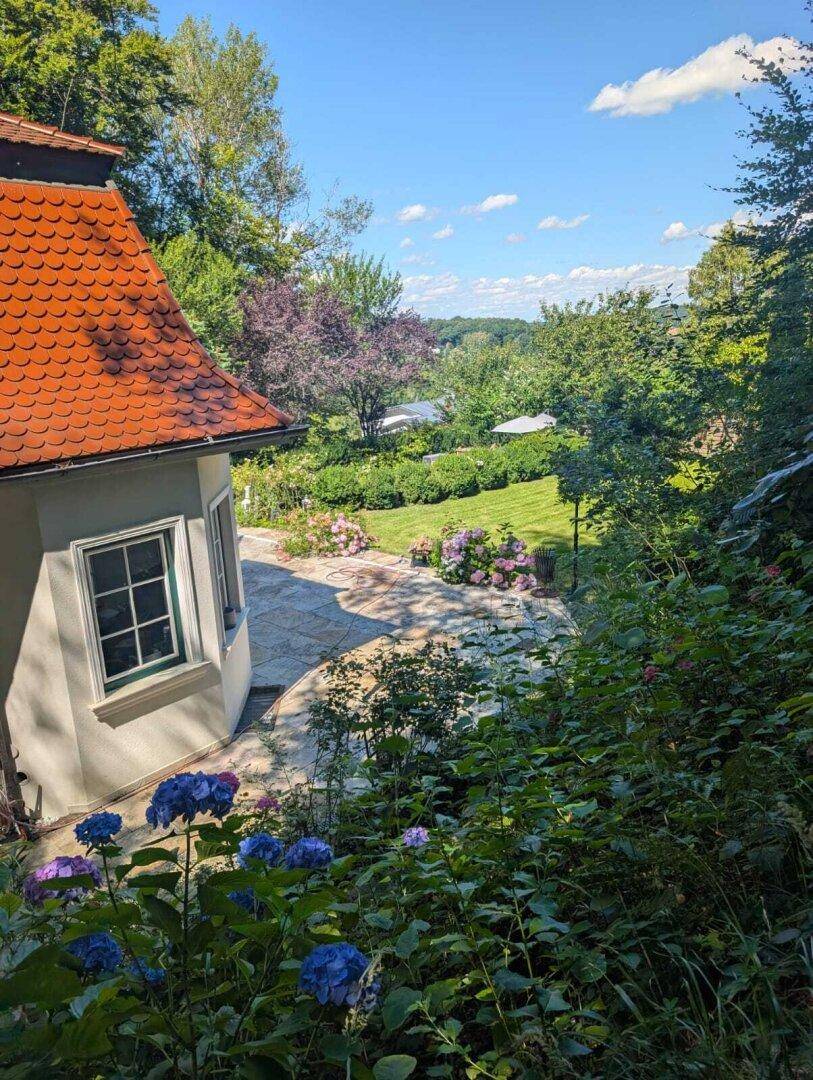 Hausansicht mit Garten und weitem Blick über die grüne Hügellandschaft.