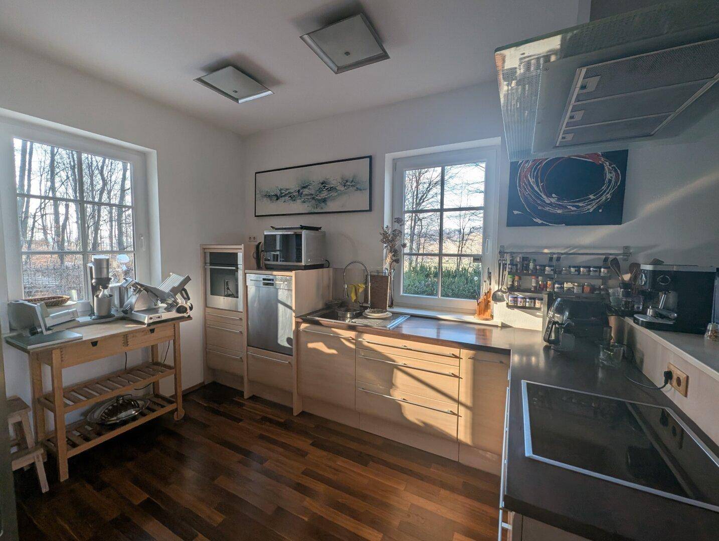 Lichtdurchflutete Küche mit Holzfronten, modernen Geräten und sonnigem Ausblick.