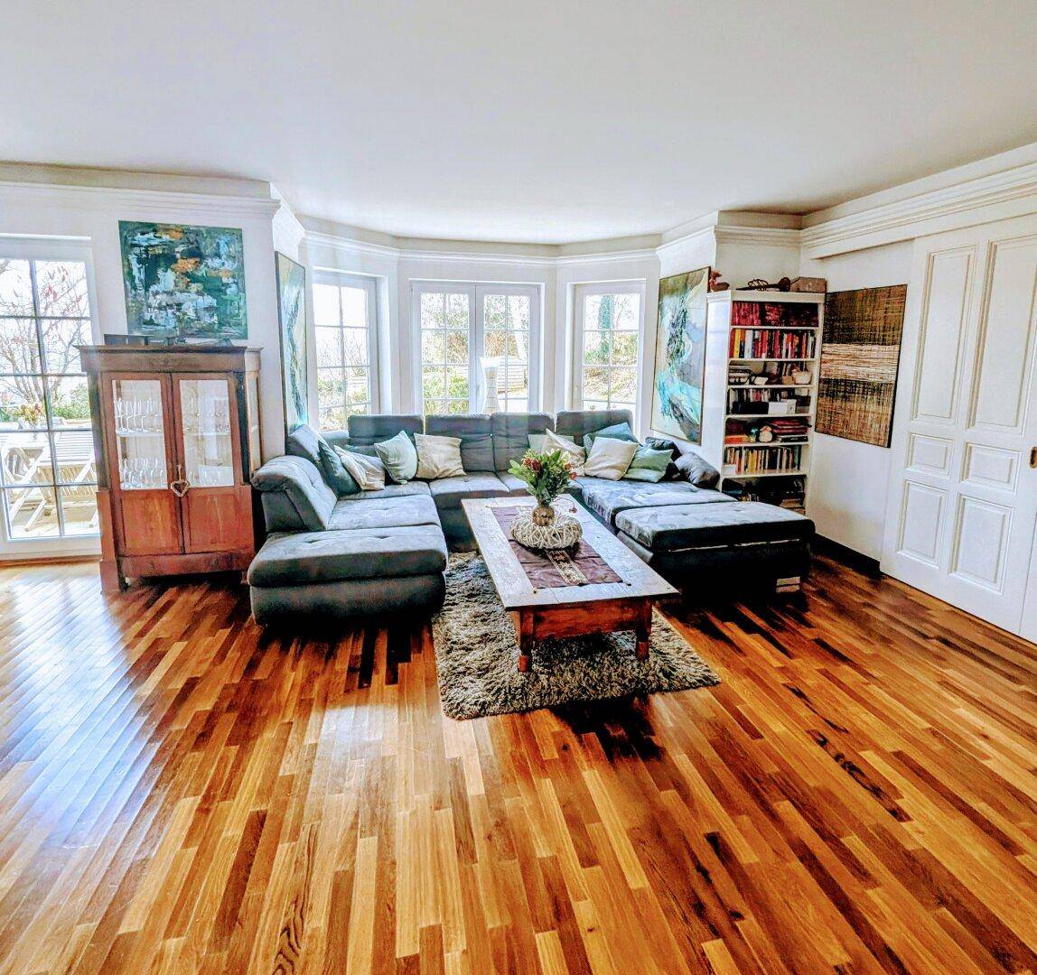 Geräumiges Wohnzimmer mit großer Eckcouch, Parkettboden und hellen Fenstern.