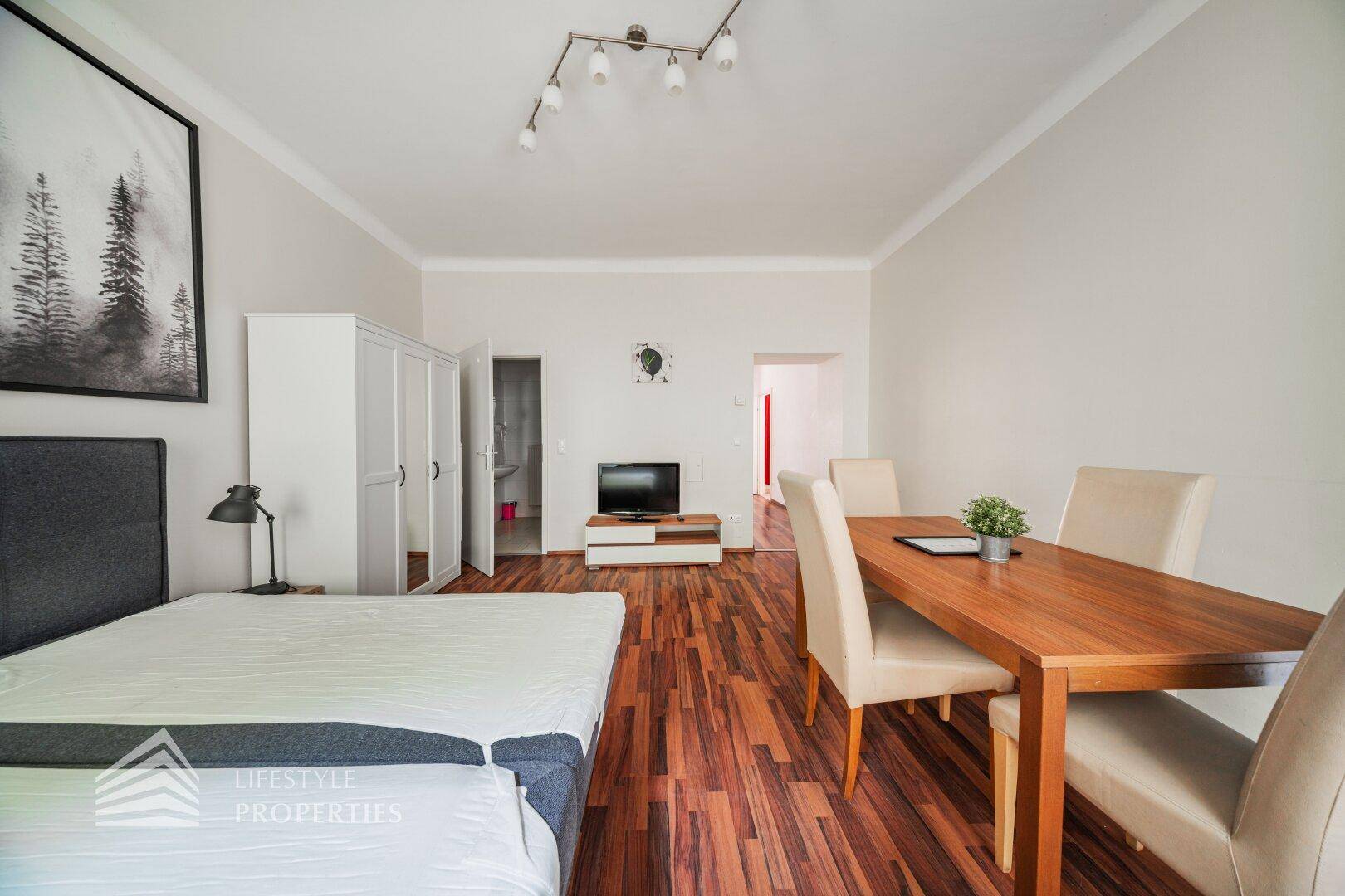Geräumiges Wohn-Schlafzimmer mit Essbereich, Holzboden und schlichtem Dekor.