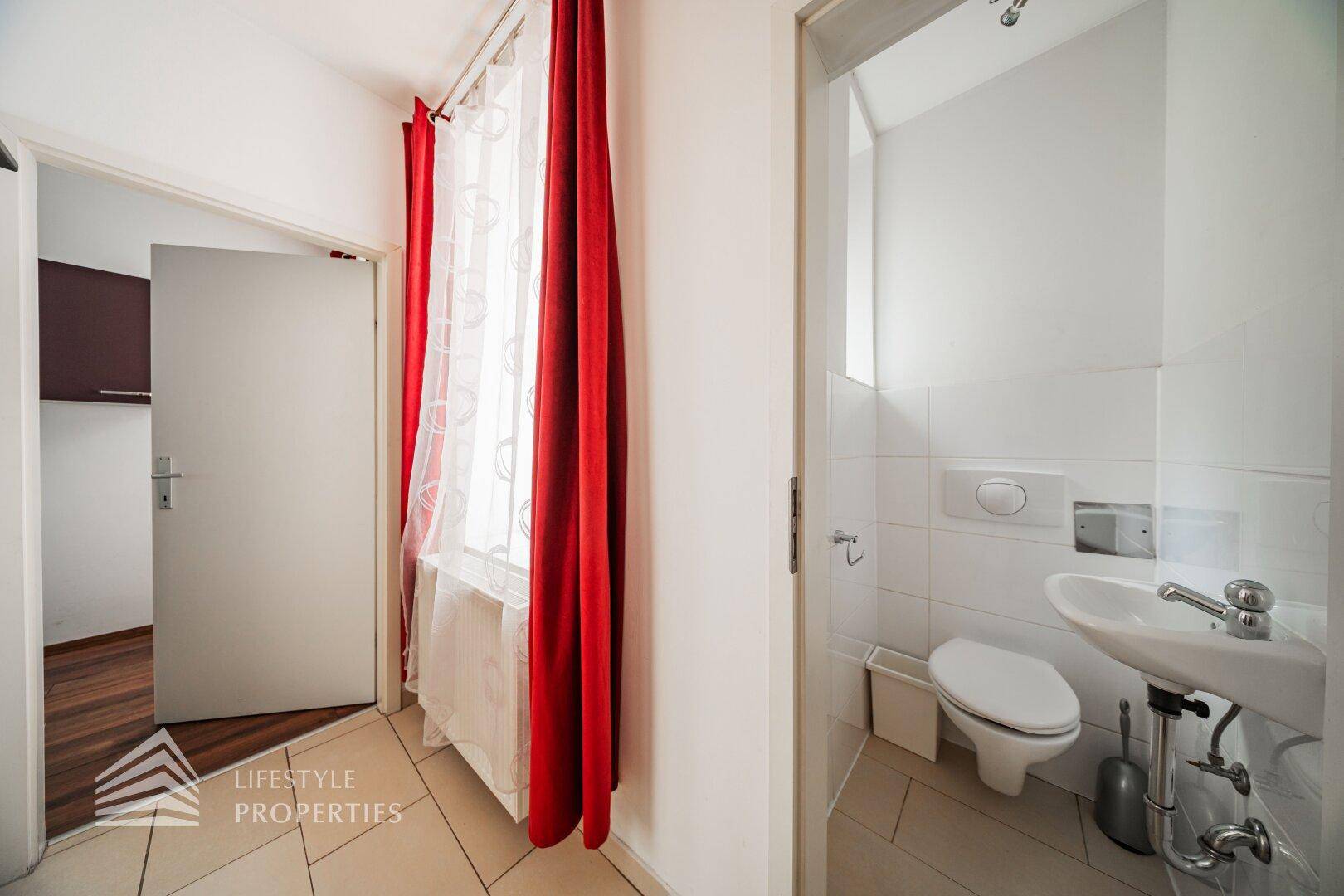 Kleines Gäste-WC mit Wand-WC, Waschbecken und Fliesenboden.