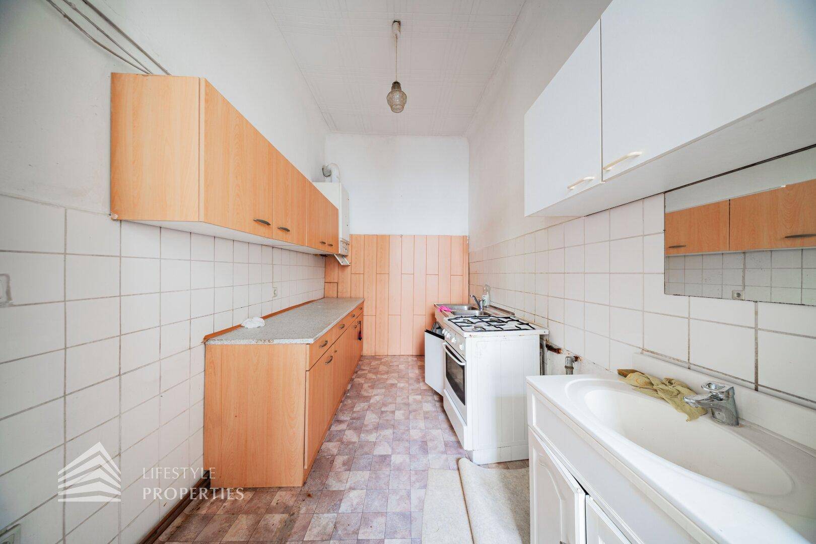 Einfache Küche mit Holzschränken, Fliesenrückwand und Gasherd, in renovierungsbedürftigem Zustand.