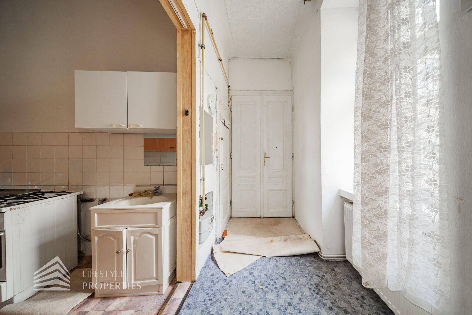 Eingangsbereich mit Teppichboden und Zugang zur Küche, renovierungsbedürftig und einfach gehalten.