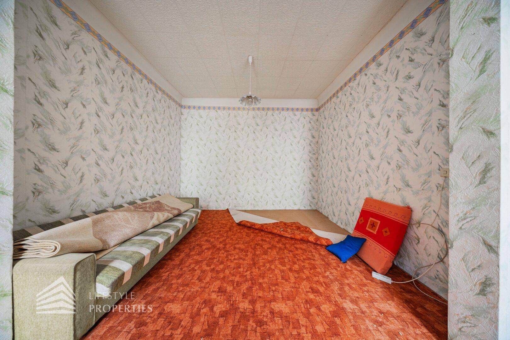 Unmöbliertes Zimmer mit gemusterter Tapete und Teppichboden, bereit zur Renovierung und Neugestaltung.