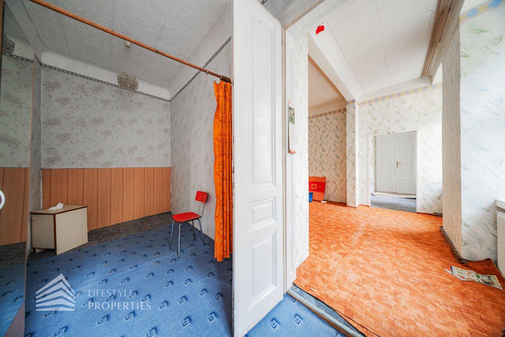 Flur mit blauem Teppich und Blick in ein angrenzendes Zimmer mit orangefarbenem Bodenbelag.