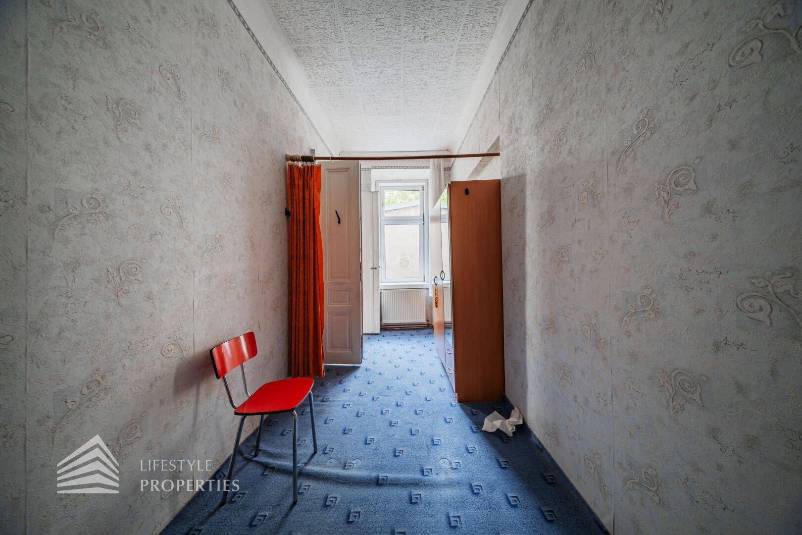 Schmaler Flur mit blauem Teppichboden, Kleiderschrank und Fenster am Ende, in einfachem Stil.