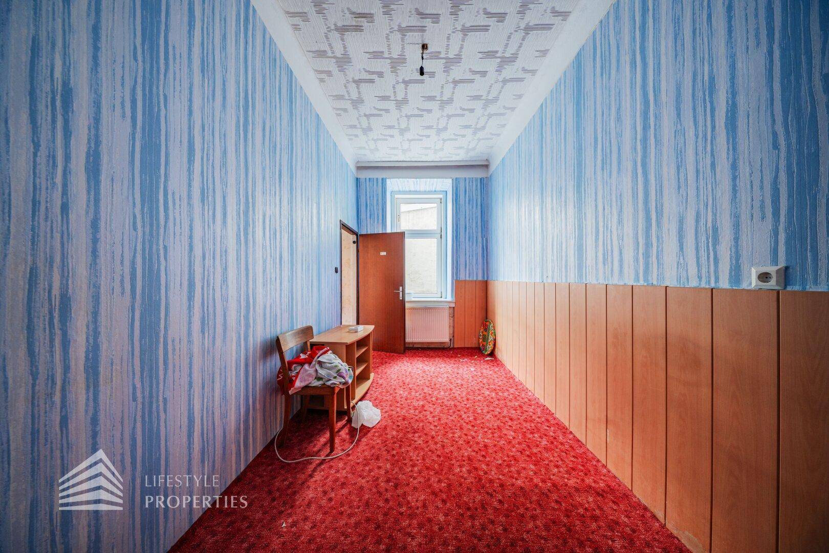 Langer Flur mit blauer Streifentapete, rotem Teppich und Holzvertäfelung, in altem Zustand.