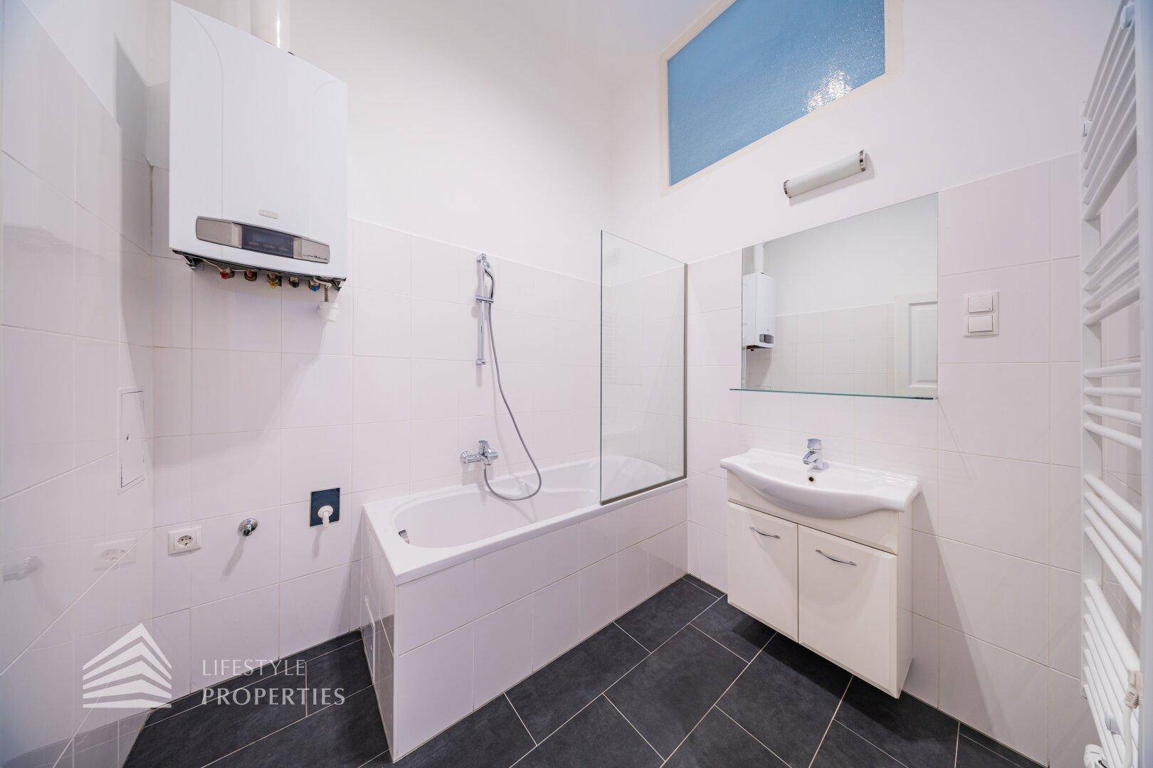 Modernes Badezimmer mit Badewanne, Dusche und Waschbecken, ausgestattet mit weißen Fliesen.