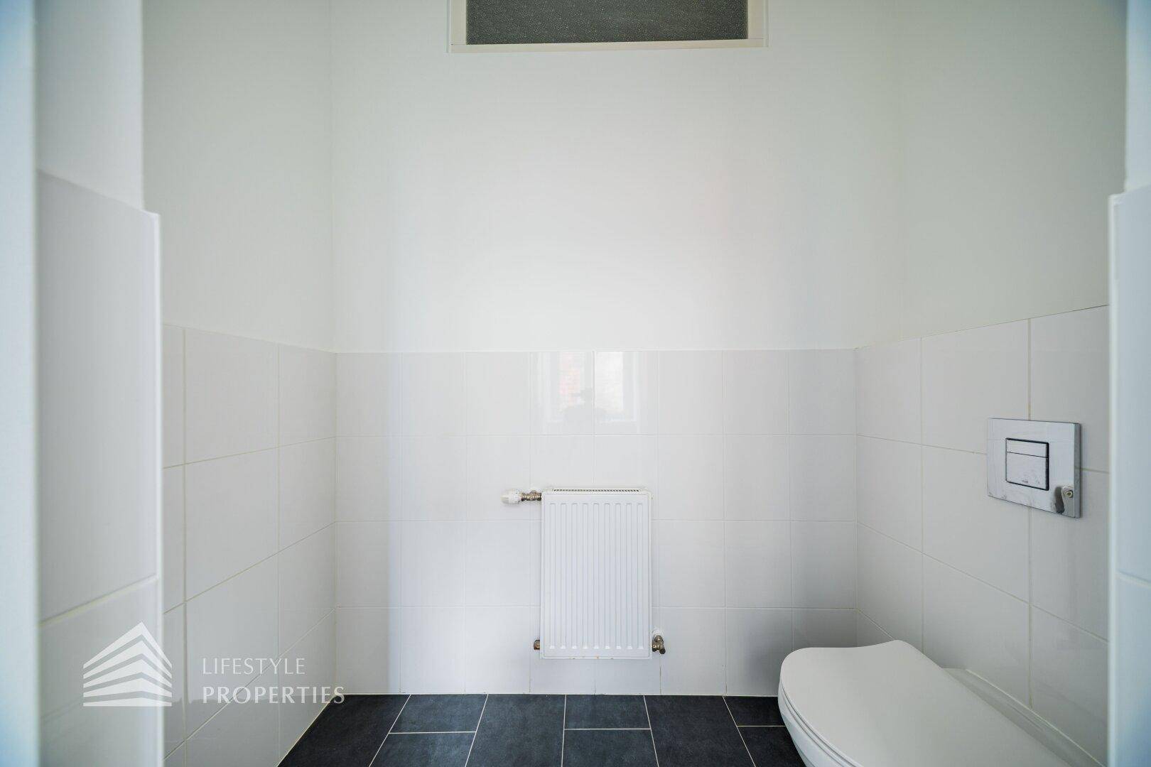 Separates WC mit Wand-WC und Heizkörper, ausgestattet mit weißen Wandfliesen.