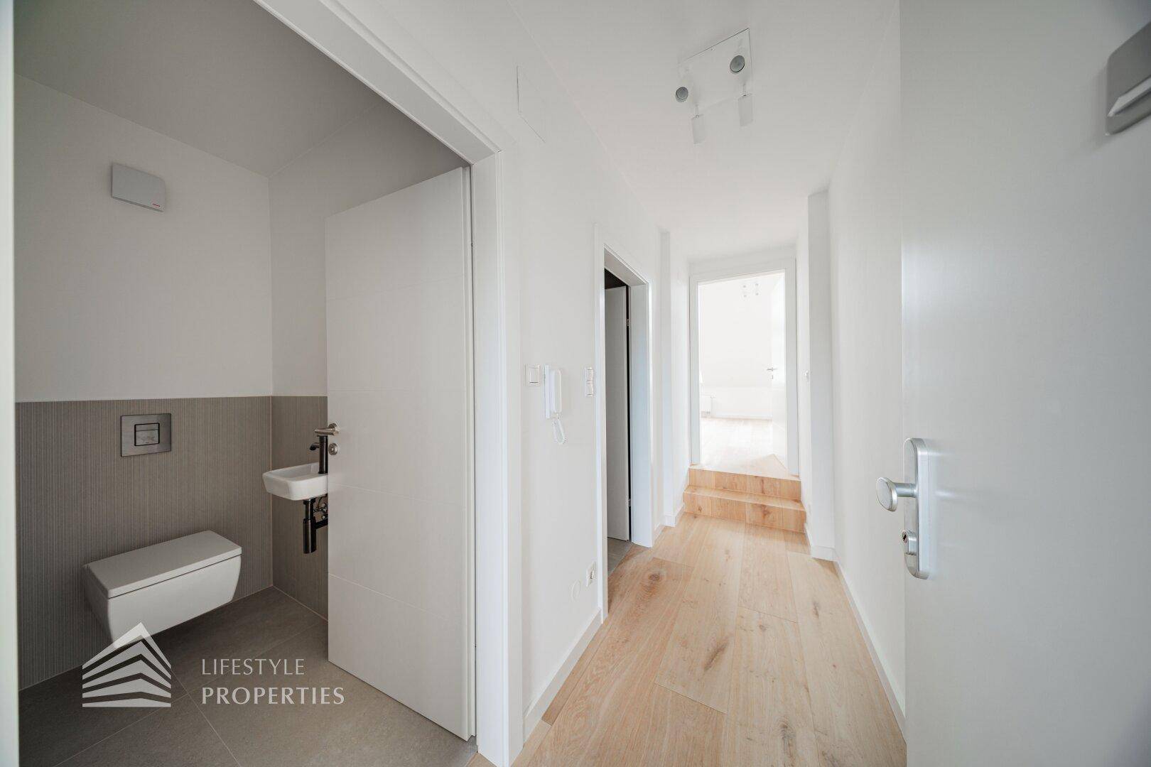 Heller Flur mit Holzfußboden und Zugang zu einem modernen Gäste-WC mit Wand-WC und kleinem Waschbecken.