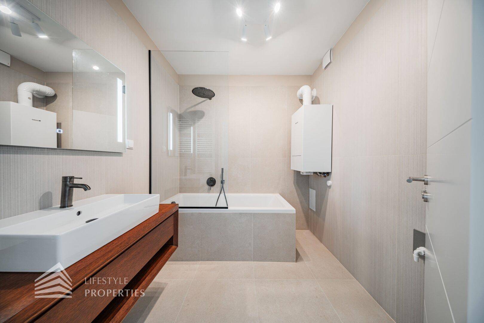 Modernes Badezimmer mit beigefarbenen Fliesen, Badewanne mit Dusche und elegantem Waschtisch mit Holzunterschrank.