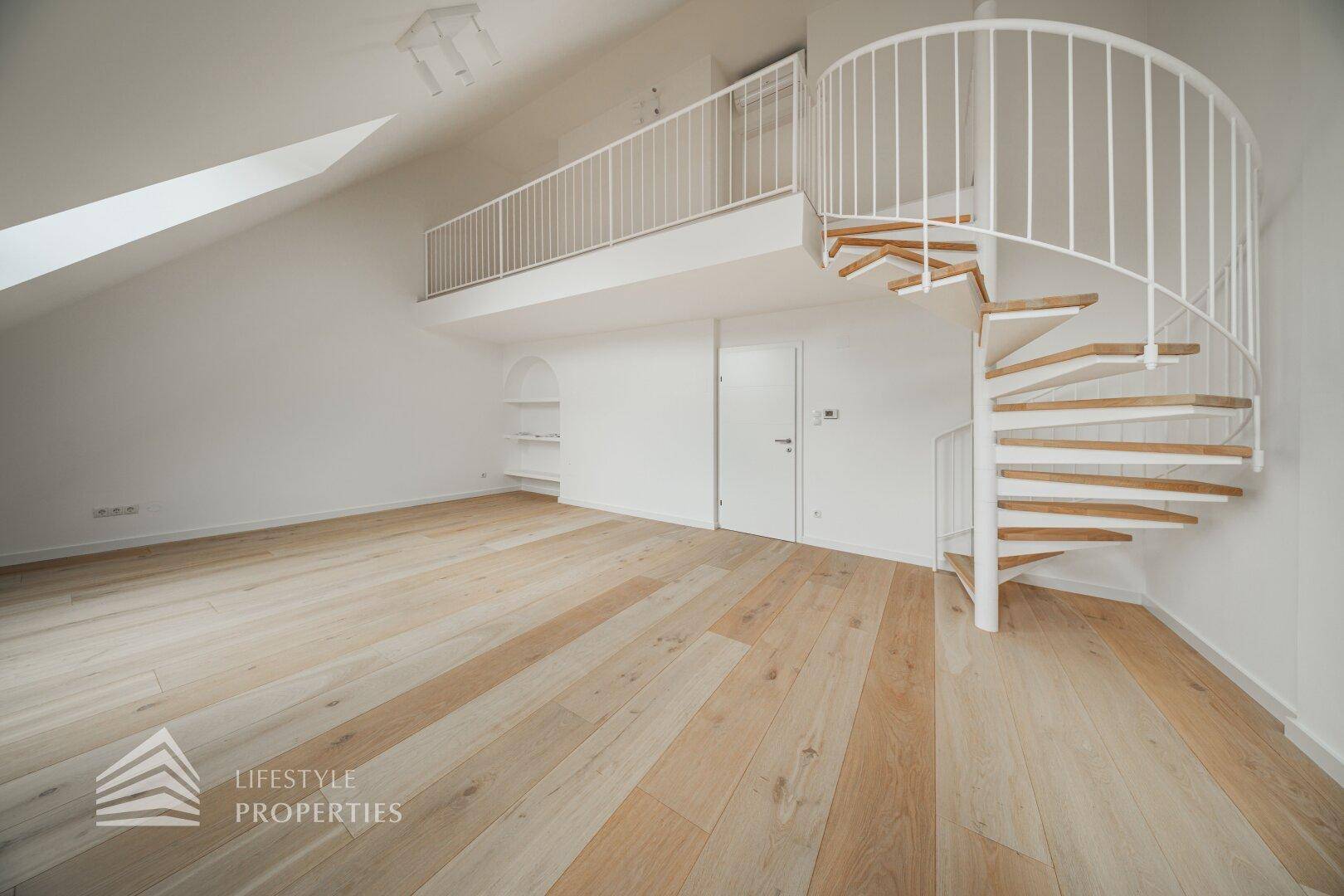 Geräumiger Wohnbereich im Dachgeschoss mit Wendeltreppe, die zu einer Galerie führt, und hellem Holzfußboden.