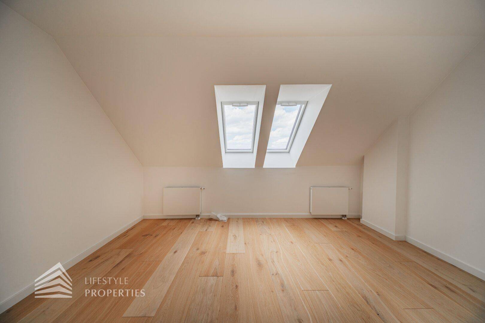 Geräumiger, heller Dachgeschossraum mit zwei großen Dachfenstern und warmem Holzfußboden.