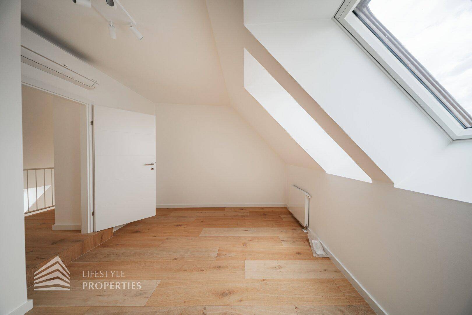 Helles Zimmer im Dachgeschoss mit Holzfußboden, Dachfenster und Klimaanlage, ideal als Schlaf- oder Arbeitszimmer.