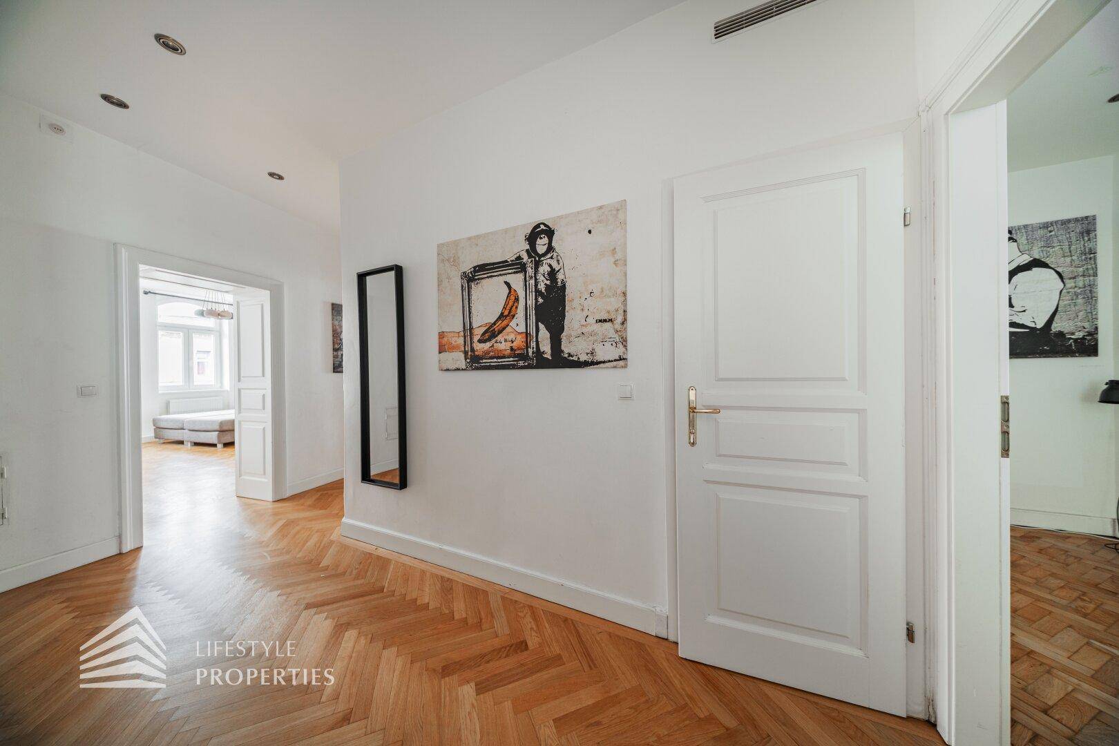 Heller Flur mit Fischgrätparkett und moderner Kunst an den weißen Wänden.