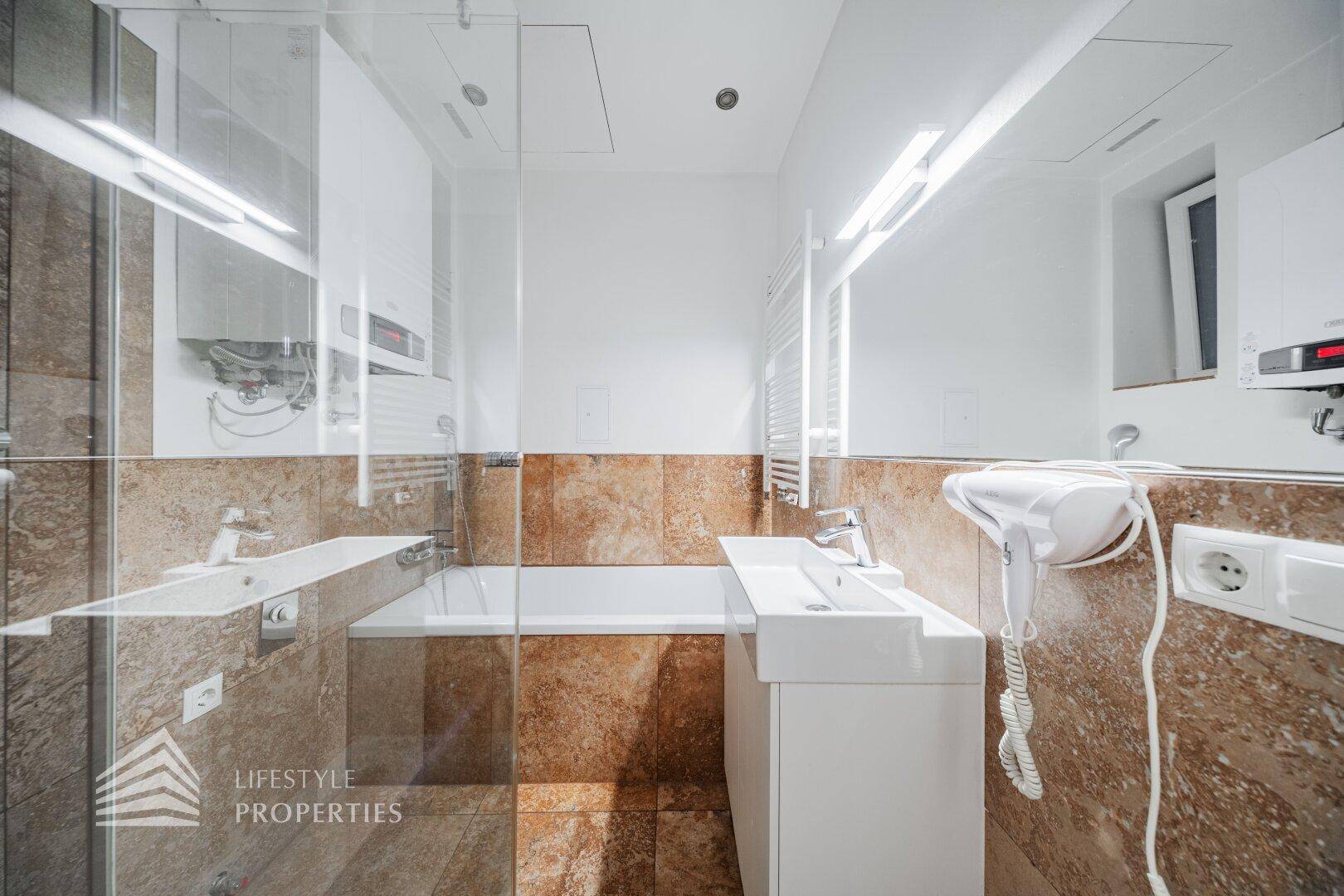 Modernes Badezimmer mit Badewanne, Einzelwaschbecken und braunen Steinfliesen an Wänden und Boden.