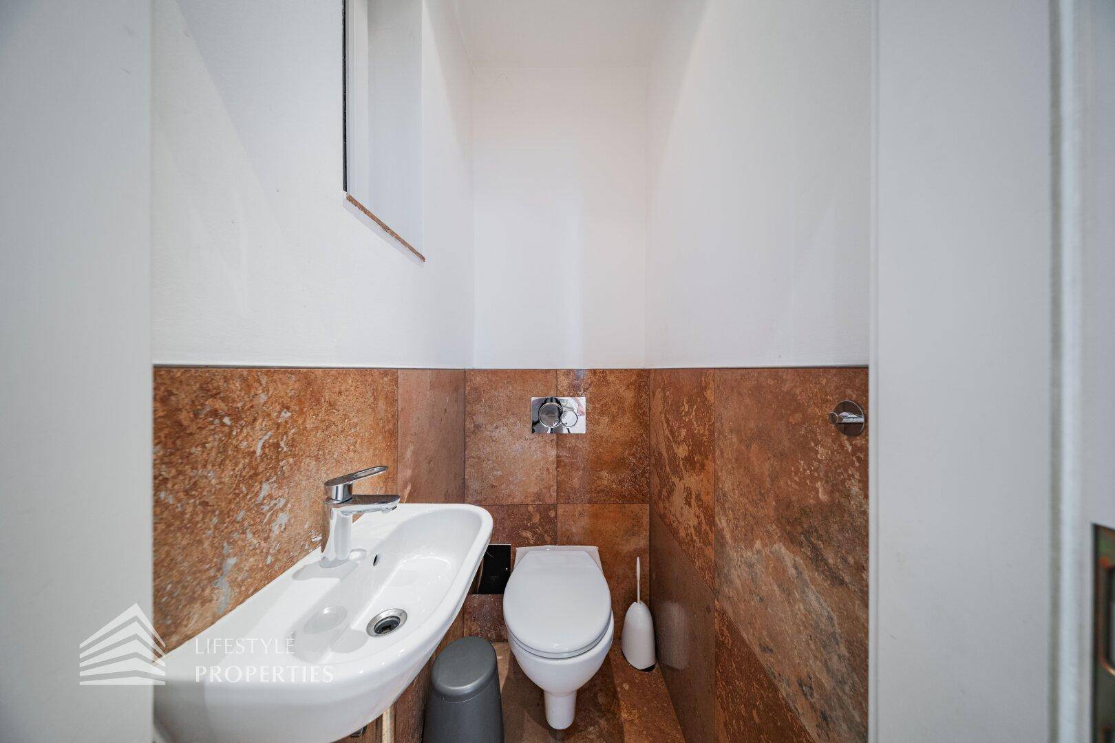 Separates Gäste-WC mit kleinem Waschbecken und braunen Steinfliesen an der Wand.