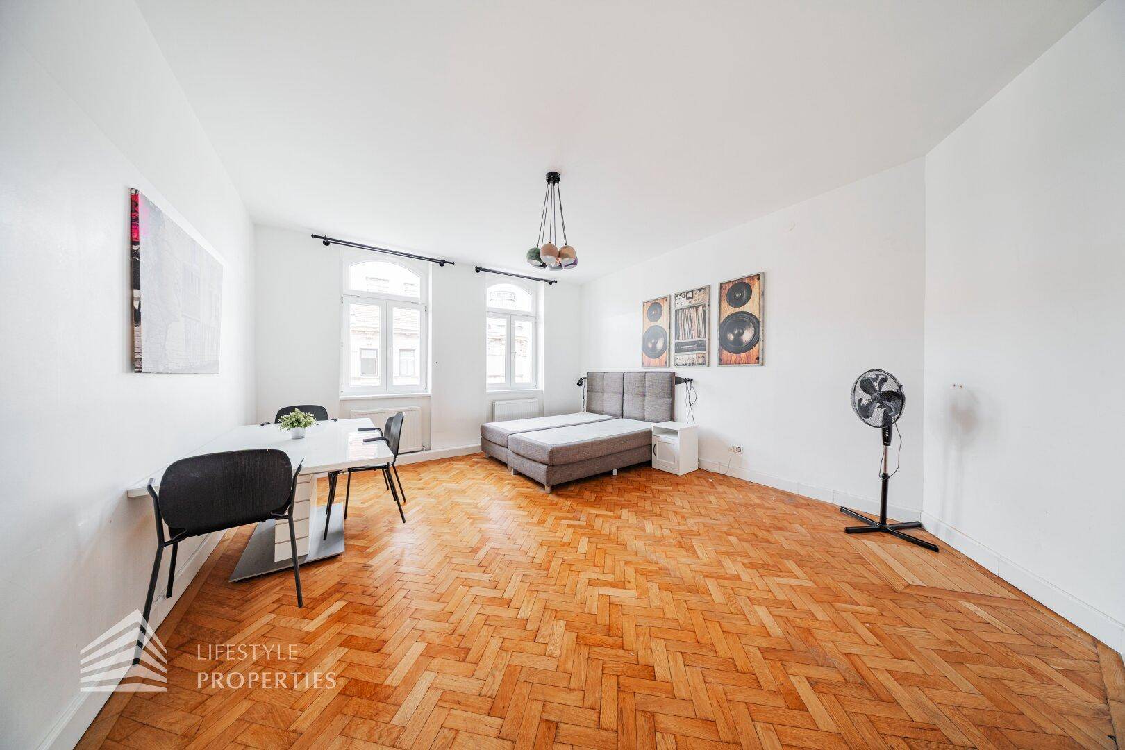 Großes Schlafzimmer mit Doppelbett, kleinem Essbereich und klassischem Fischgrätparkett.