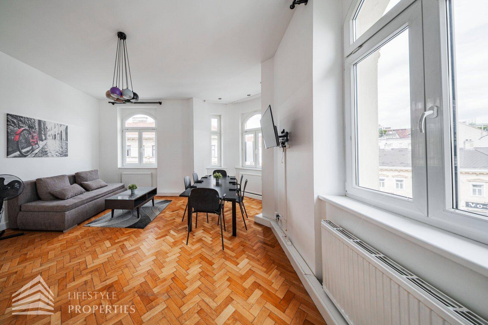 Geräumiger Wohn-Essbereich mit Parkettboden und Blick auf die Stadt durch die großen Fenster.