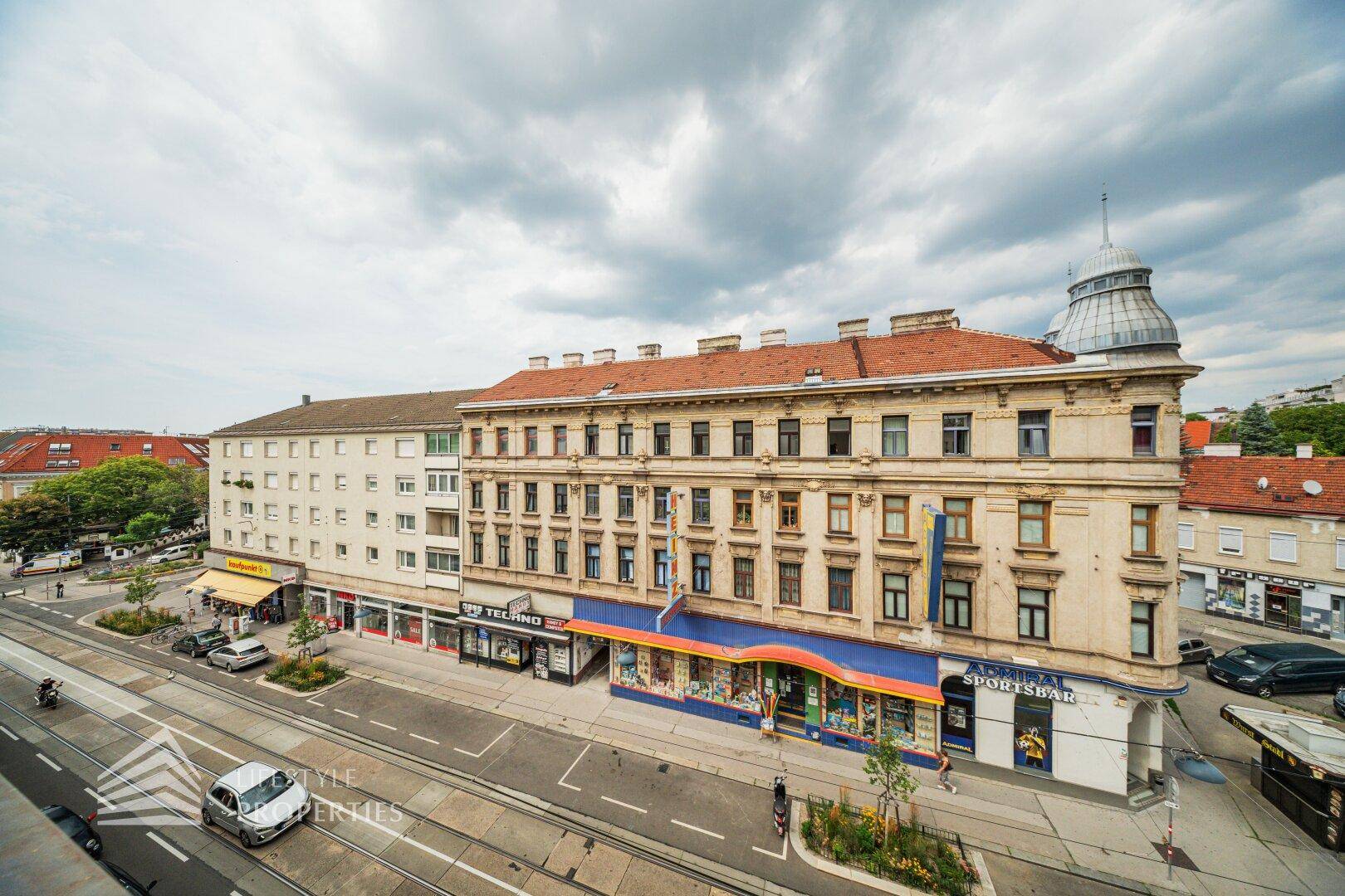 Blick von oben auf eine belebte Stadtstraße mit historischen Gebäuden und Straßenbahnschienen.