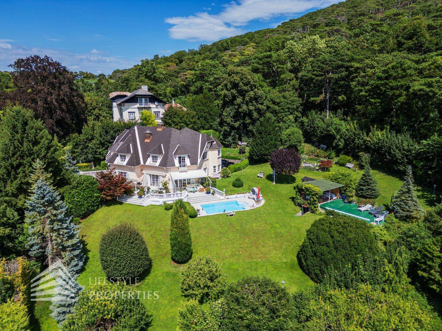 Panoramablick auf die elegante Villa mit Pool, weitläufigem Garten und bewaldeter Hügellandschaft im Hintergrund.