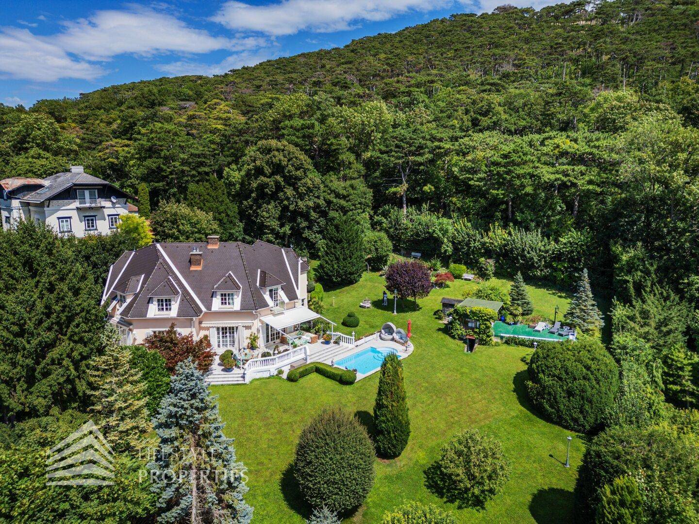 Die luxuriöse Villa eingebettet in eine grüne Landschaft mit Pool und Blick auf die bewaldeten Hügel.